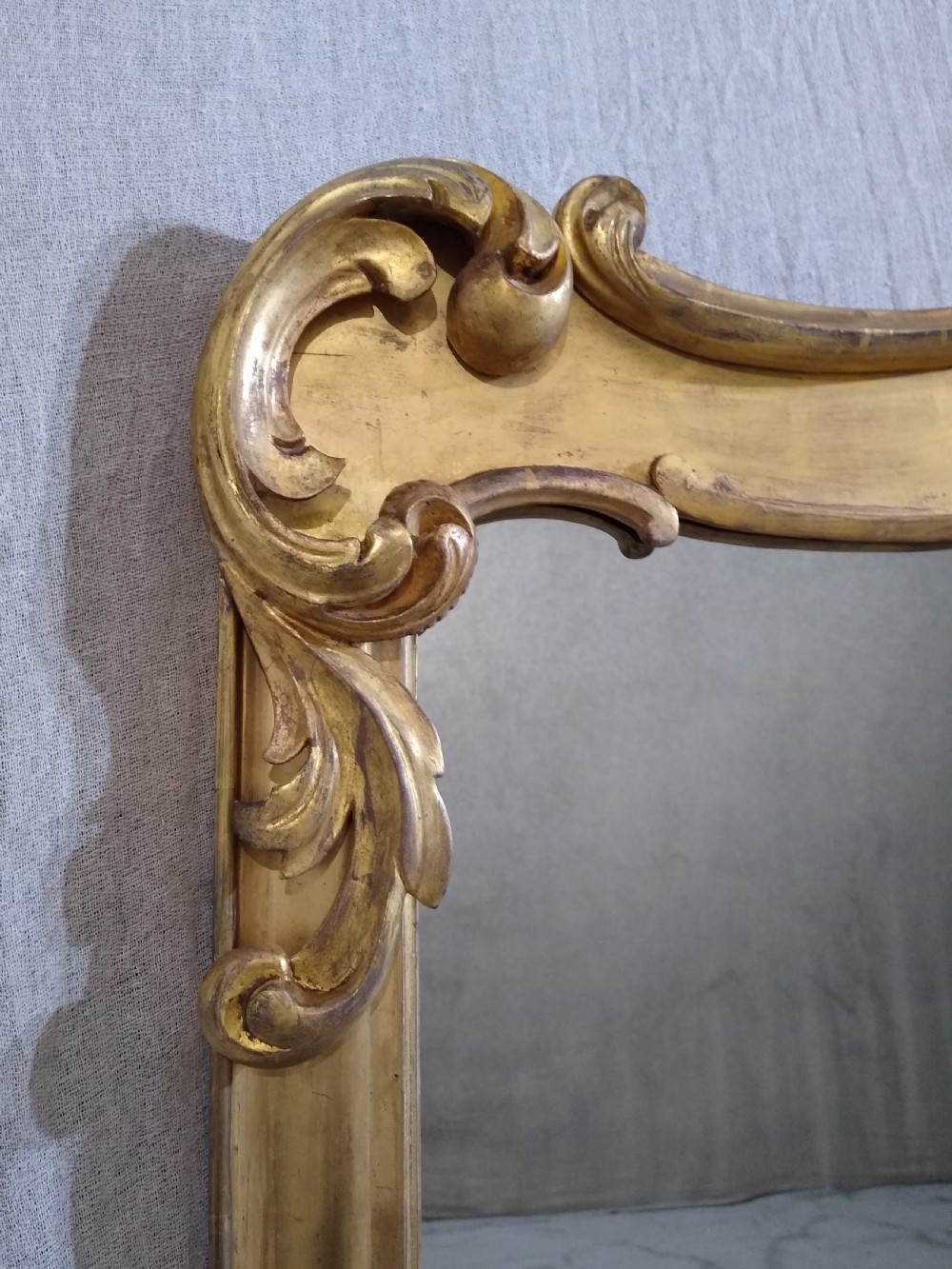 A large mid-nineteenth century giltwood overmantel mirror featuring elaborate scrolled cresting and decorative corner accents. View II