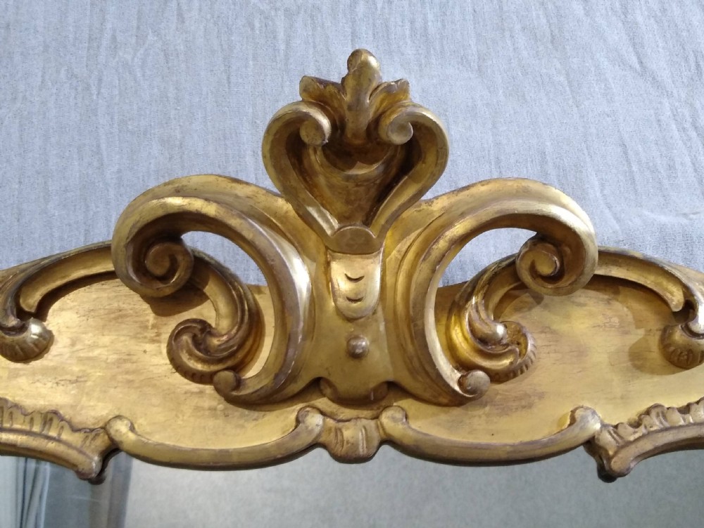 A large mid-nineteenth century giltwood overmantel mirror featuring elaborate scrolled cresting and decorative corner accents. View IV