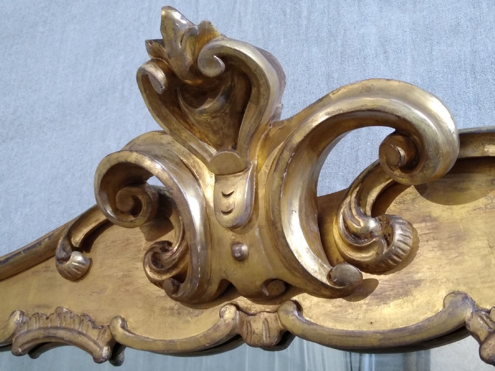 A large mid-nineteenth century giltwood overmantel mirror featuring elaborate scrolled cresting and decorative corner accents. View V