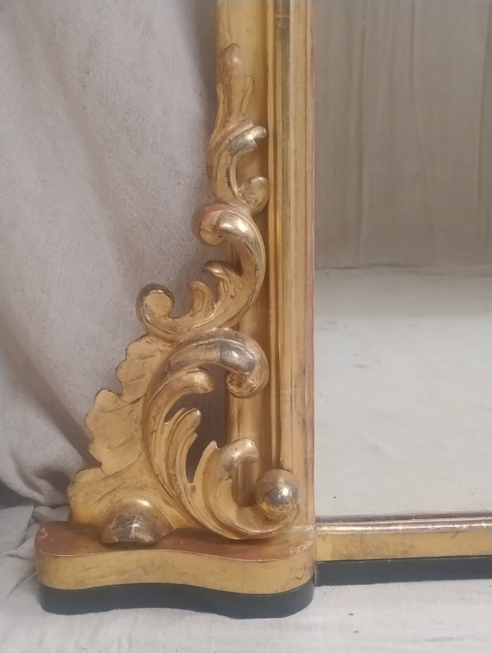 A large arched antique overmantel mirror featuring a gold giltwood frame with carved acanthus leaf scrolls at the lower corners. View III