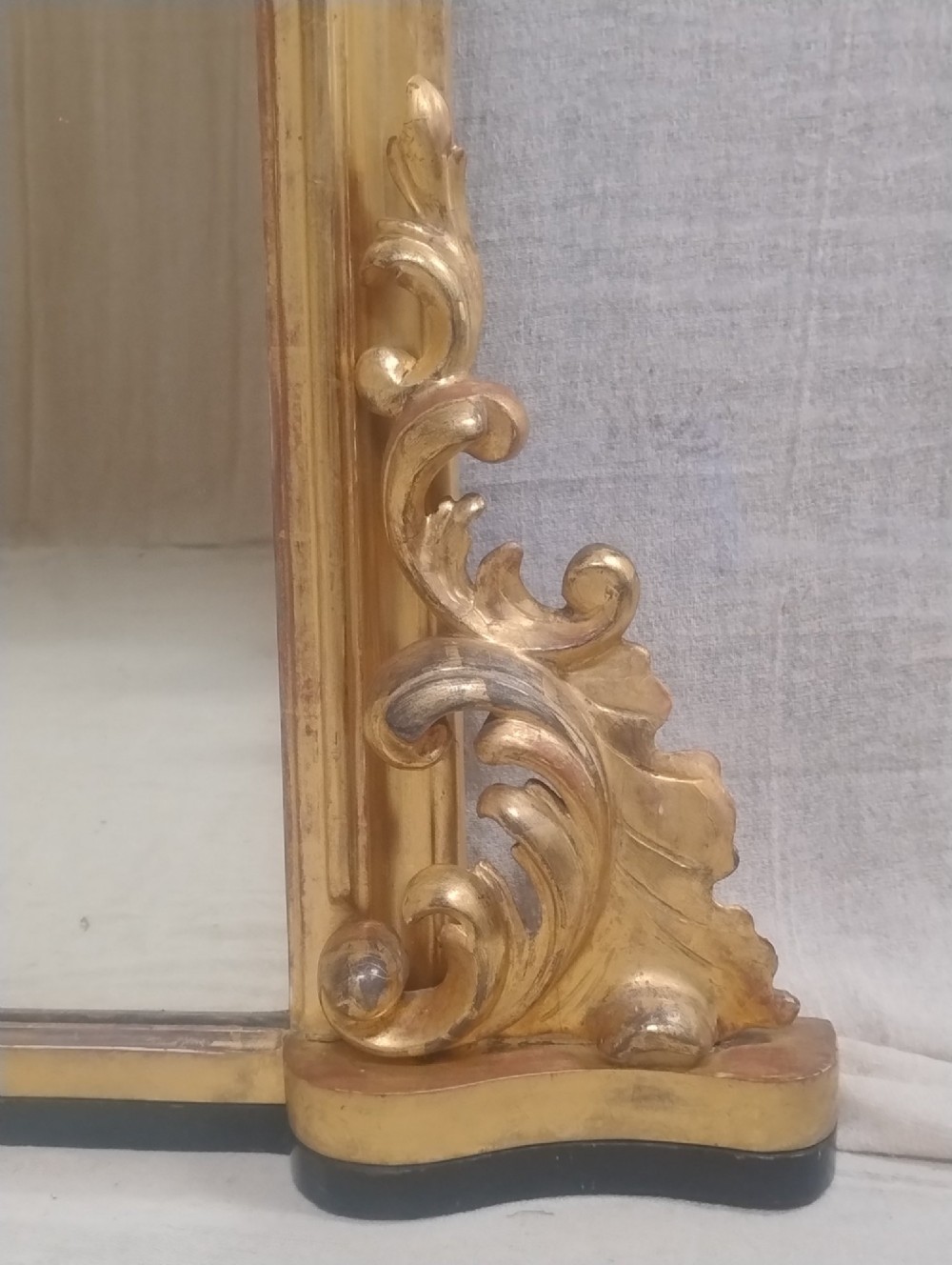 A large arched antique overmantel mirror featuring a gold giltwood frame with carved acanthus leaf scrolls at the lower corners. View IV