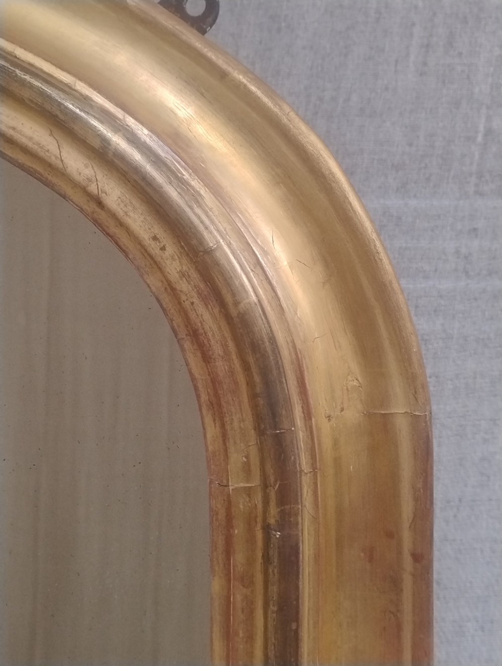 A large arched antique overmantel mirror featuring a gold giltwood frame with carved acanthus leaf scrolls at the lower corners. View VI