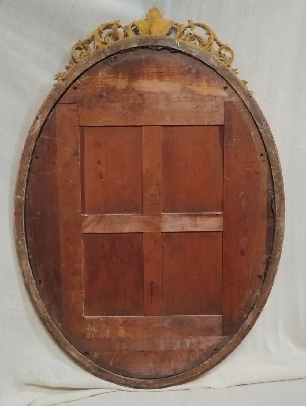 An antique oval wall mirror featuring a giltwood frame topped with an ornate leaf cresting and enclosing a mercury glass plate. View II