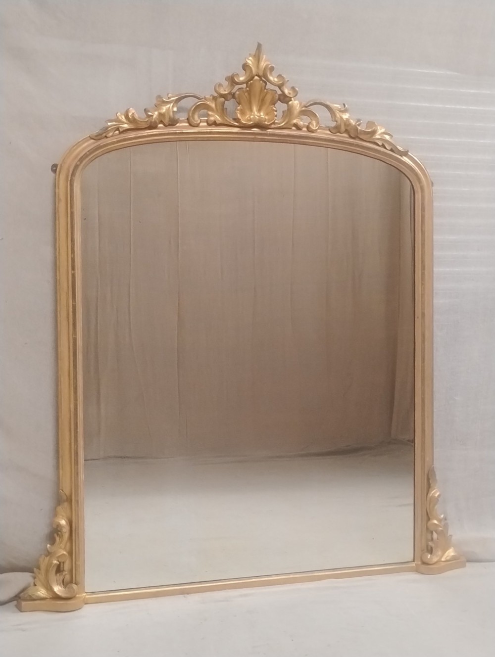 An arched Victorian overmantel mirror with a gilded finish, decorated with a central carved shell crest and scrolled side feet.