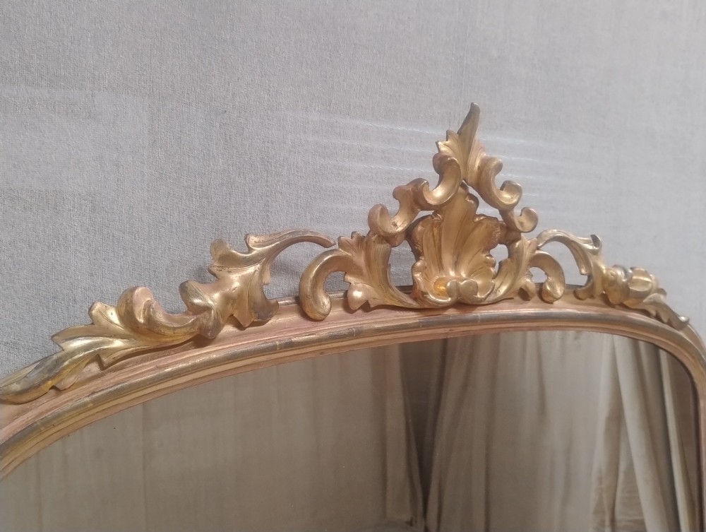 An arched Victorian overmantel mirror with a gilded finish, decorated with a central carved shell crest and scrolled side feet. View VII
