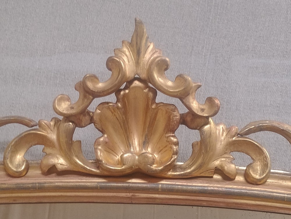 An arched Victorian overmantel mirror with a gilded finish, decorated with a central carved shell crest and scrolled side feet. View VIII