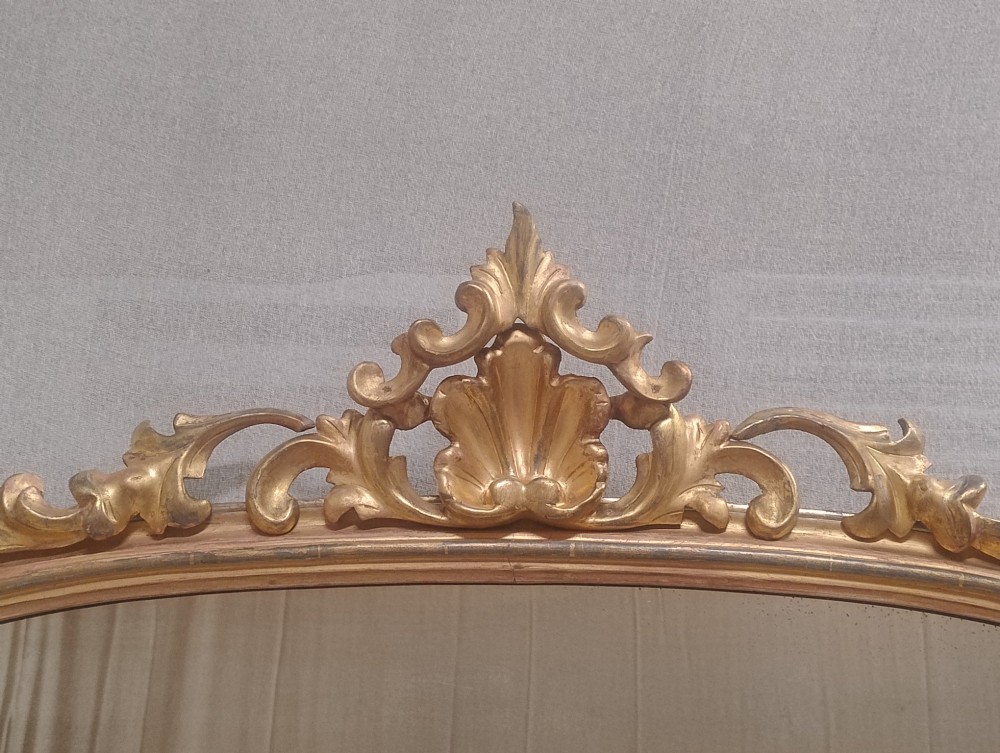An arched Victorian overmantel mirror with a gilded finish, decorated with a central carved shell crest and scrolled side feet. View IX