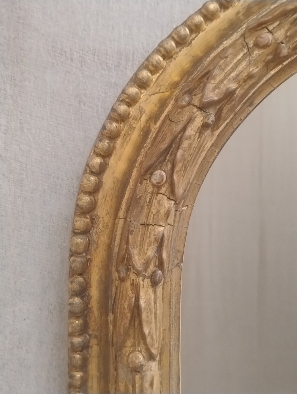 A large Victorian giltwood overmantel mirror featuring an arched top decorated with a carved ribbon bow crest and lower scrolled side supports. View V