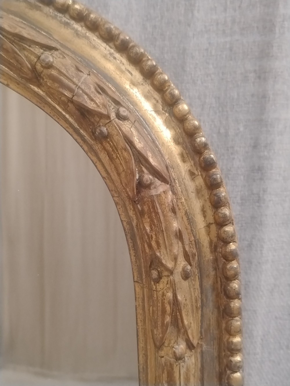 A large Victorian giltwood overmantel mirror featuring an arched top decorated with a carved ribbon bow crest and lower scrolled side supports. View VI