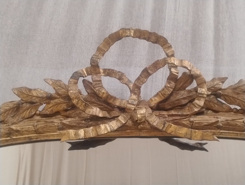 A large Victorian giltwood overmantel mirror featuring an arched top decorated with a carved ribbon bow crest and lower scrolled side supports. View VIII