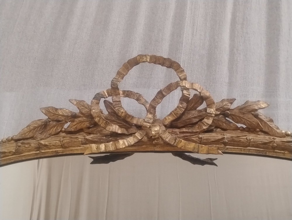 A large Victorian giltwood overmantel mirror featuring an arched top decorated with a carved ribbon bow crest and lower scrolled side supports. View IX