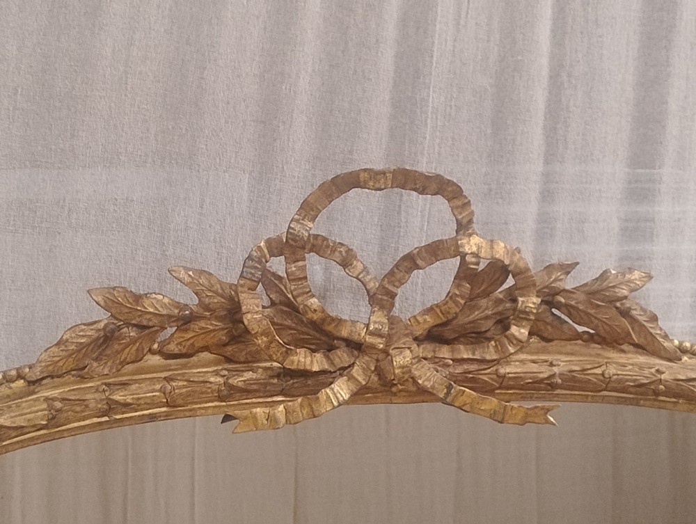 A large Victorian giltwood overmantel mirror featuring an arched top decorated with a carved ribbon bow crest and lower scrolled side supports. View X