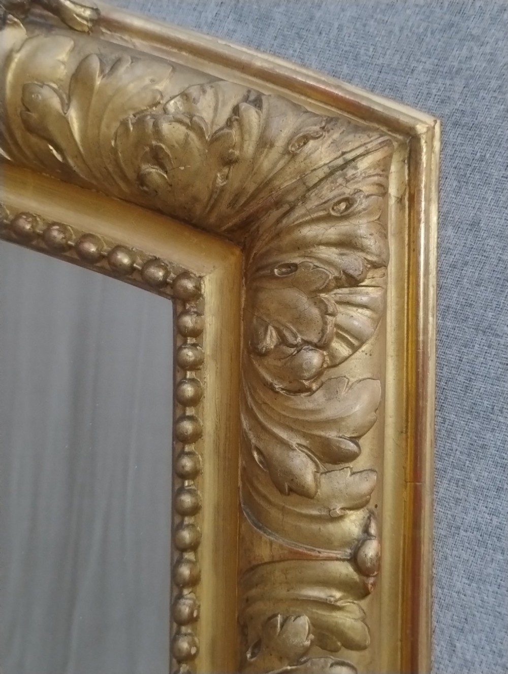 A tall French giltwood mirror featuring a carved floral cartouche cresting, arched top, and moulded beaded inner border. View II