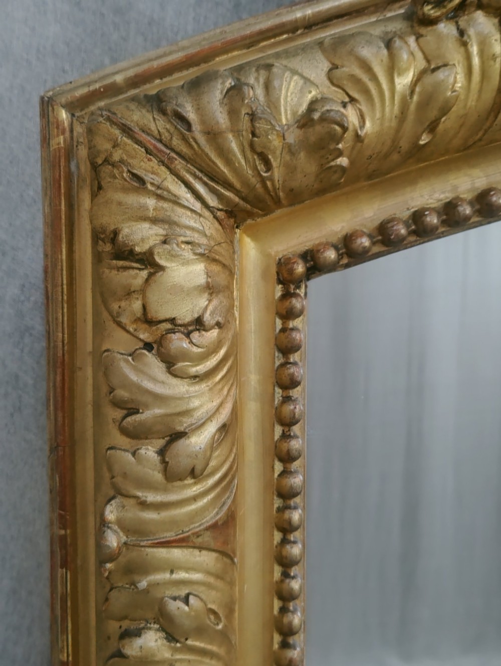 A tall French giltwood mirror featuring a carved floral cartouche cresting, arched top, and moulded beaded inner border. View III