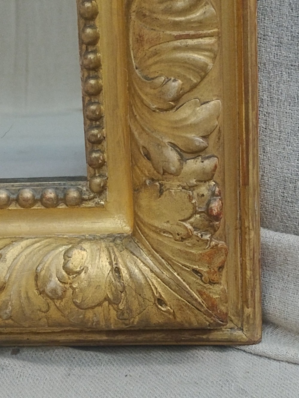 A tall French giltwood mirror featuring a carved floral cartouche cresting, arched top, and moulded beaded inner border. View V