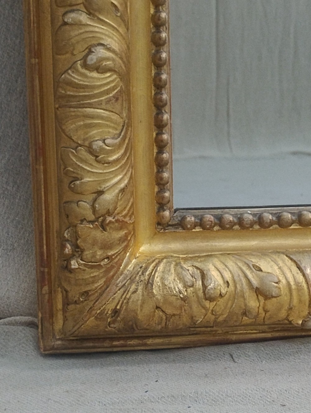 A tall French giltwood mirror featuring a carved floral cartouche cresting, arched top, and moulded beaded inner border. View VI