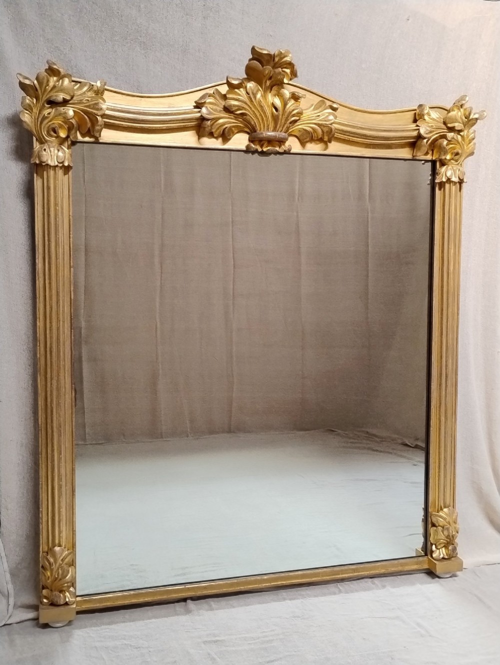 A large nineteenth-century giltwood overmantel mirror featuring carved acanthus leaf cresting and fluted column pilasters.