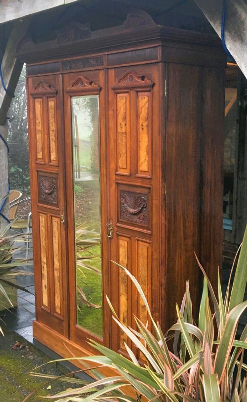 fig 1. A late Victorian double wardrobe in warm brown walnut featuring a central full-length mirrored door flanked by two carved and burr walnut panelled doors beneath a moulded pediment.