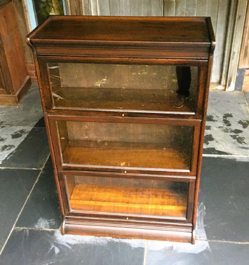 fig 1. A three-tier dark oak sectional bookcase with glazed lift-up doors and small brass knobs on a moulded base.