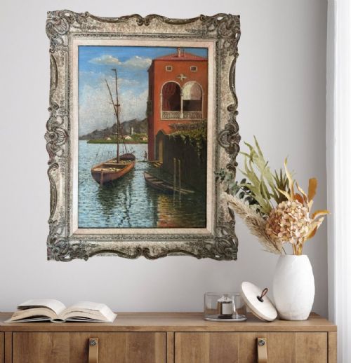 fig 2. An impressionist oil painting depicting a sailboat and small rowboat anchored beside a terracotta building along a river, presented in a carved ornate frame.