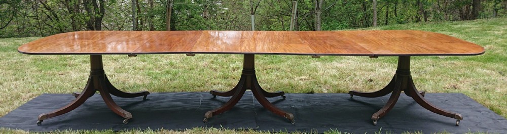 A large mahogany triple pedestal dining table with reeded legs, brass castors, and a polished extending tabletop. View X