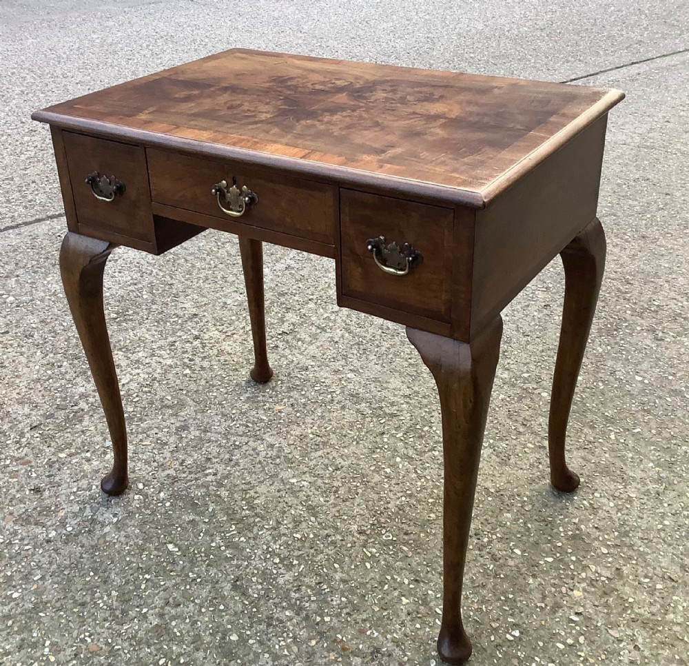 An antique Edwardian walnut lowboy featuring three drawers, brass backplate handles, cabriole legs with pad feet, and a burr walnut veneered top surface.