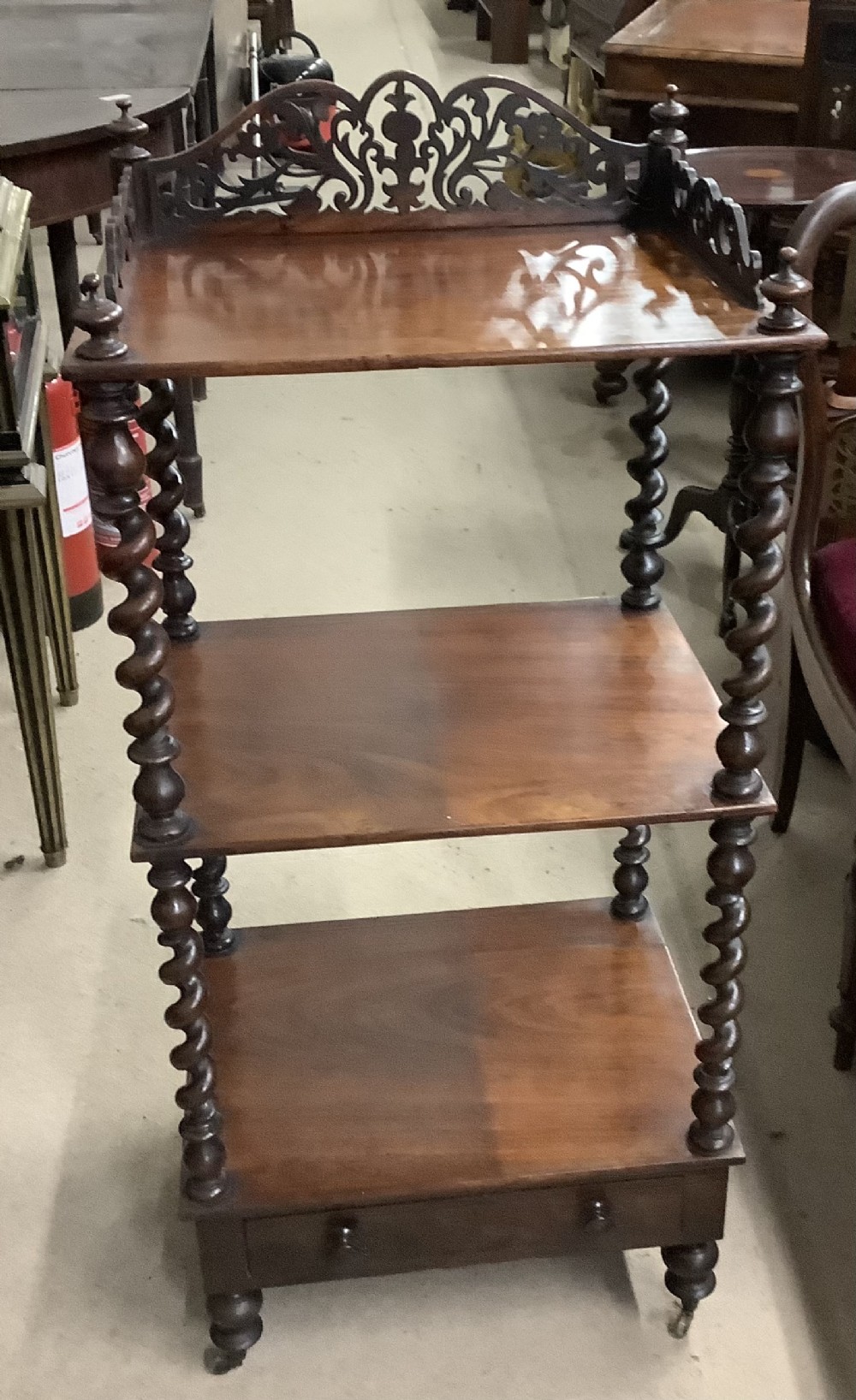 A Victorian dark wood three-tier whatnot featuring a decorative fretwork gallery, spiralled barley twist corner posts, a base drawer, and brass castors.