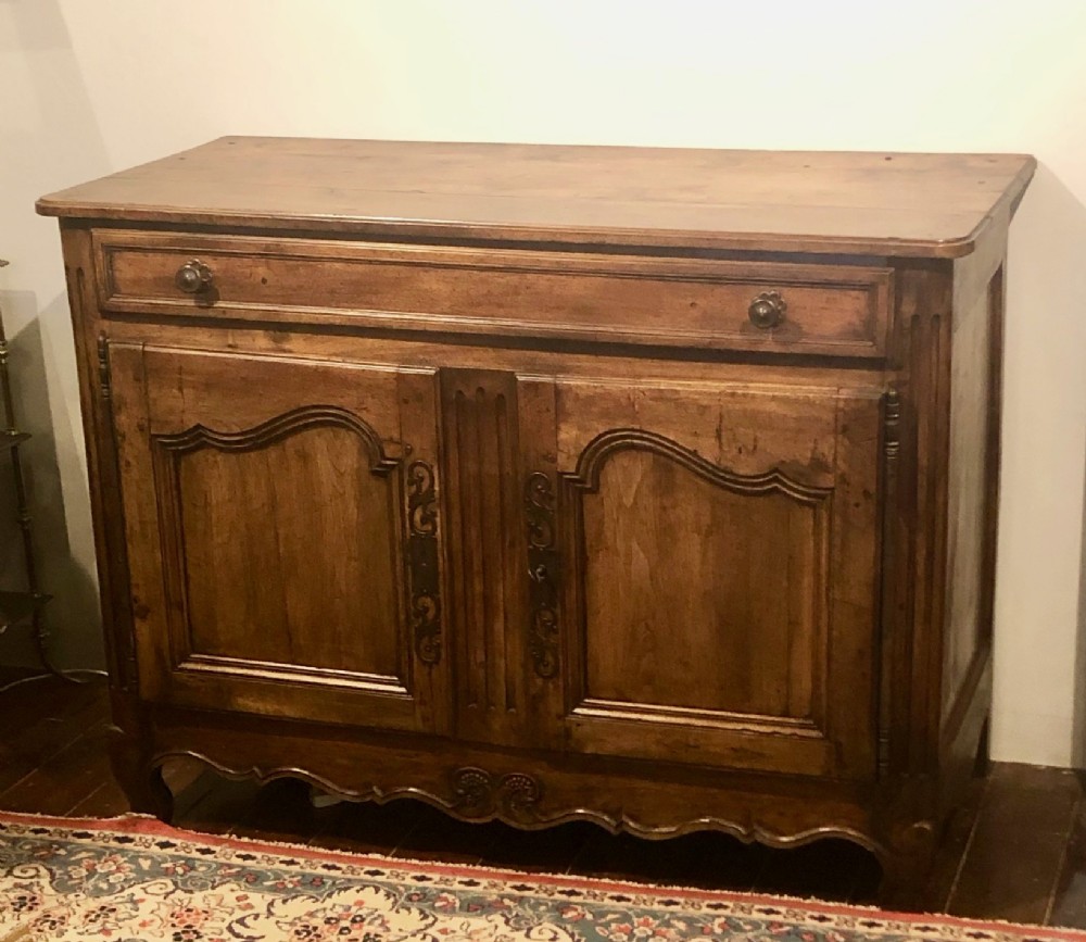 An 18th-century French provincial walnut buffet cabinet featuring a wide top drawer over two carved panelled doors with iron escutcheons and a shaped apron.