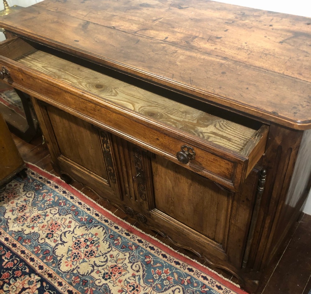 An 18th-century French provincial walnut buffet cabinet featuring a wide top drawer over two carved panelled doors with iron escutcheons and a shaped apron. View II