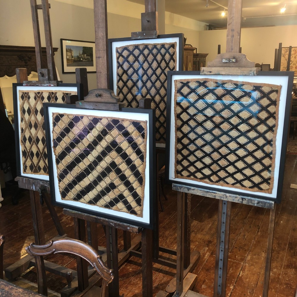 A framed geometric Kuba raffia textile featuring a diagonal grid pattern in natural tan and dark brown tones, presented within a black wooden frame and white mount. View IV