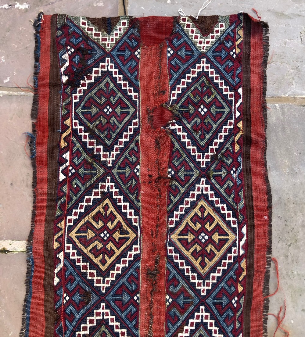 An elongated flat-woven wool textile panel featuring geometric diamond motifs in terracotta red, navy blue, green, mustard yellow, and off-white. View II