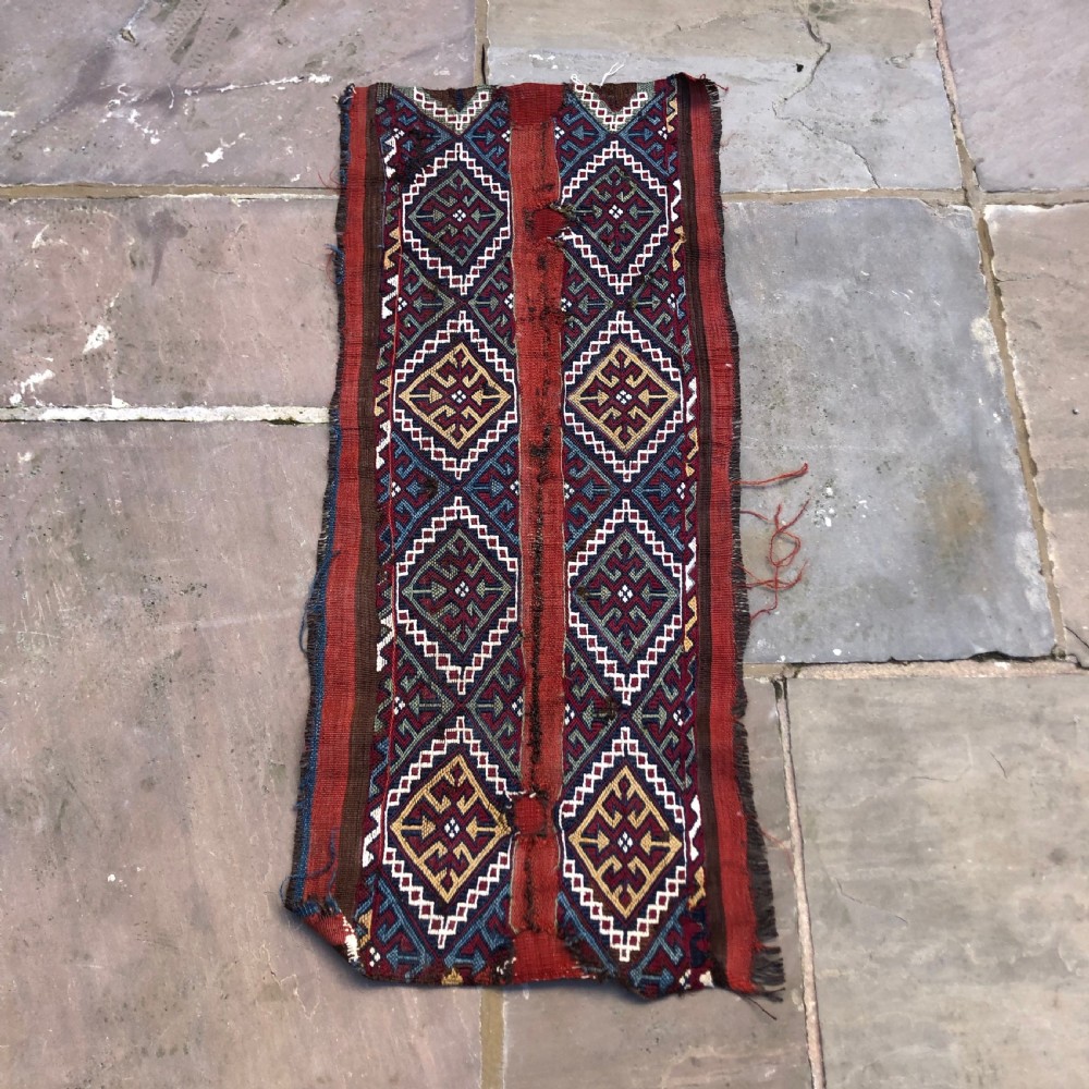 An elongated flat-woven wool textile panel featuring geometric diamond motifs in terracotta red, navy blue, green, mustard yellow, and off-white. View V