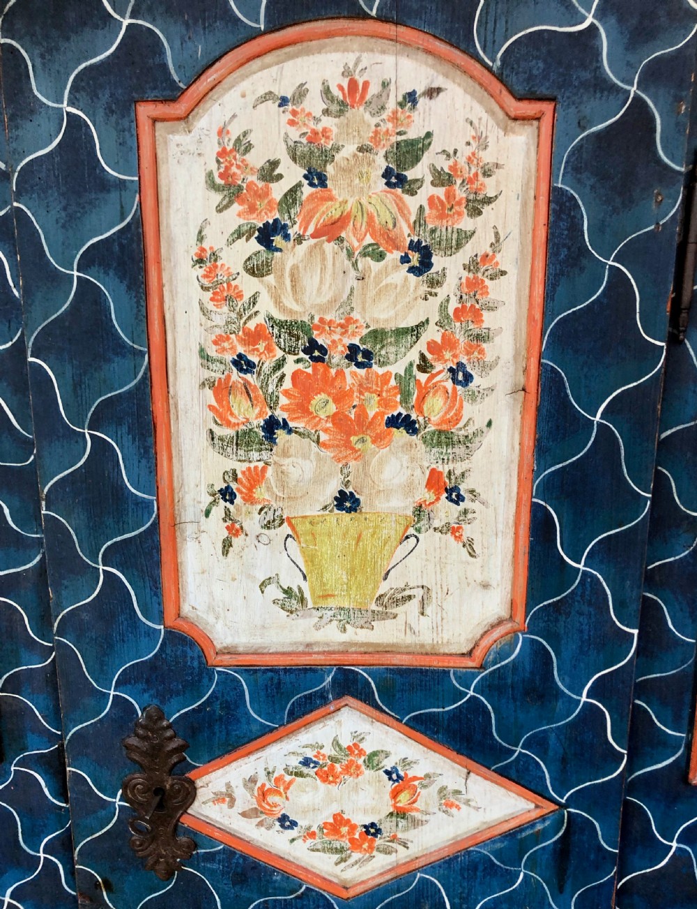 An Austro-Hungarian painted pine marriage armoire featuring a blue ground with geometric lattice motifs, hand-painted floral panels, and a shaped top cornice. View IV