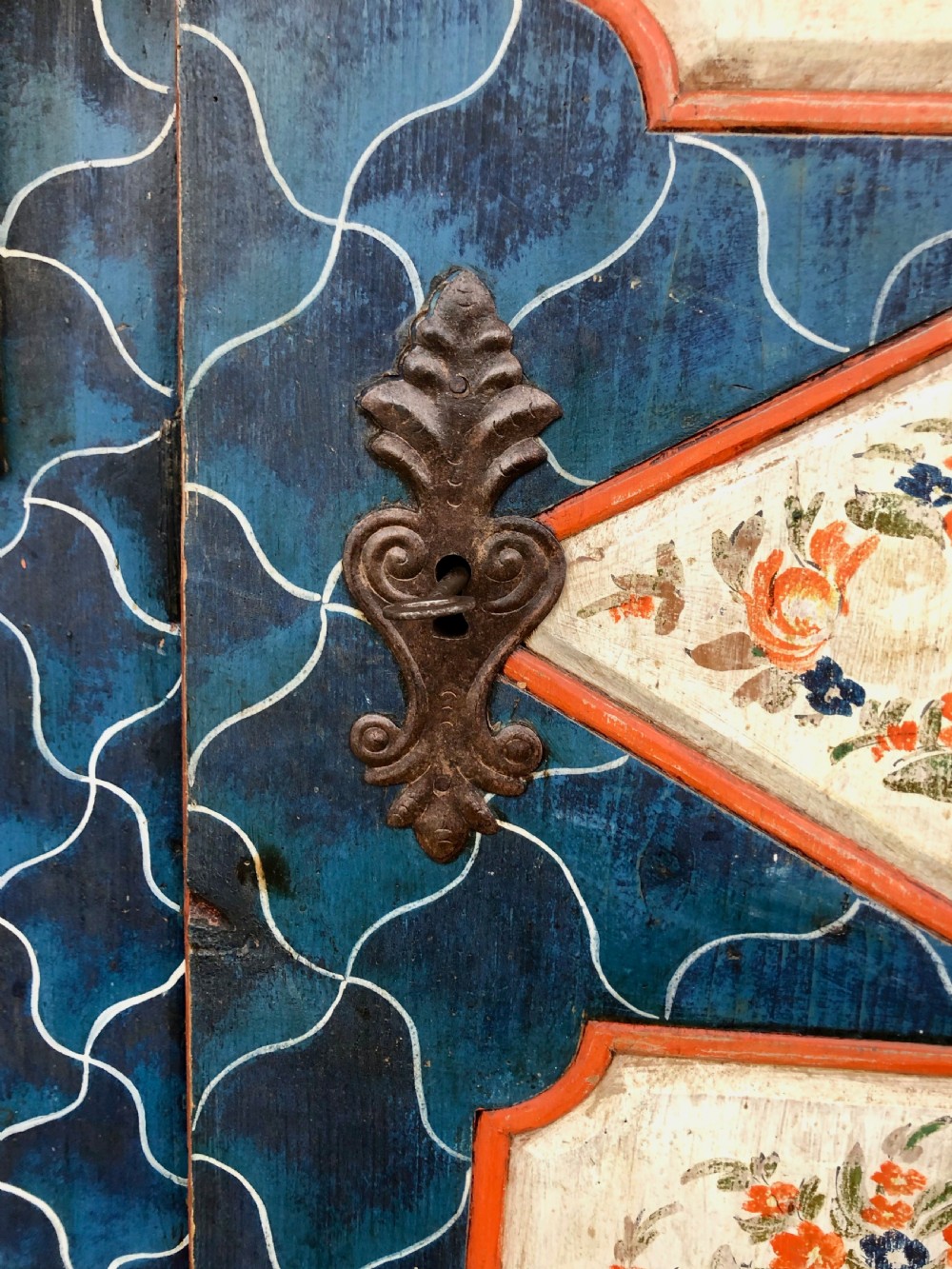 An Austro-Hungarian painted pine marriage armoire featuring a blue ground with geometric lattice motifs, hand-painted floral panels, and a shaped top cornice. View X