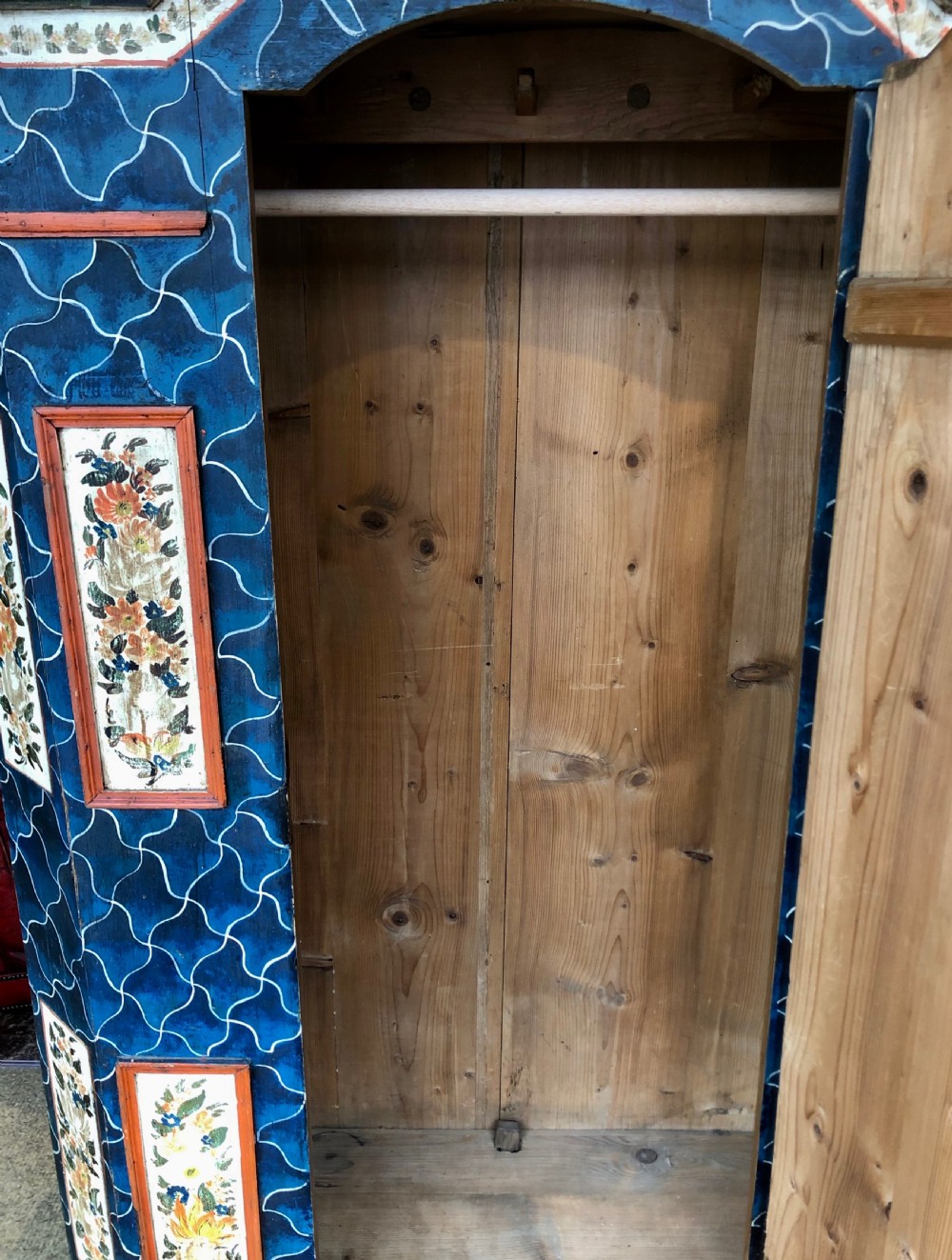 An Austro-Hungarian painted pine marriage armoire featuring a blue ground with geometric lattice motifs, hand-painted floral panels, and a shaped top cornice. View XI