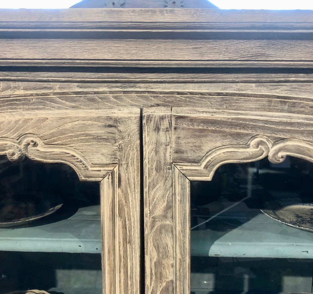 An 18th-century French limed oak vitrine featuring two glazed doors with curved frames, two lower drawers, carved floral detailing, and short cabriole feet. View III