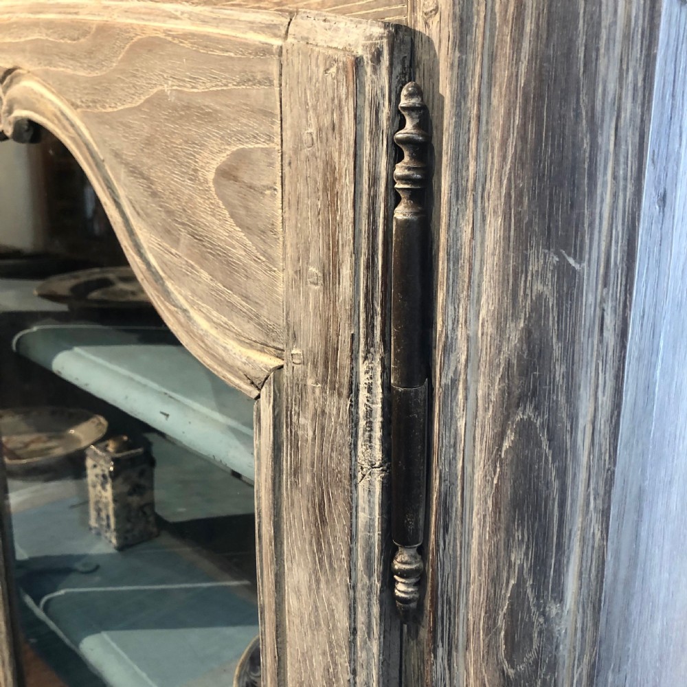 An 18th-century French limed oak vitrine featuring two glazed doors with curved frames, two lower drawers, carved floral detailing, and short cabriole feet. View VII