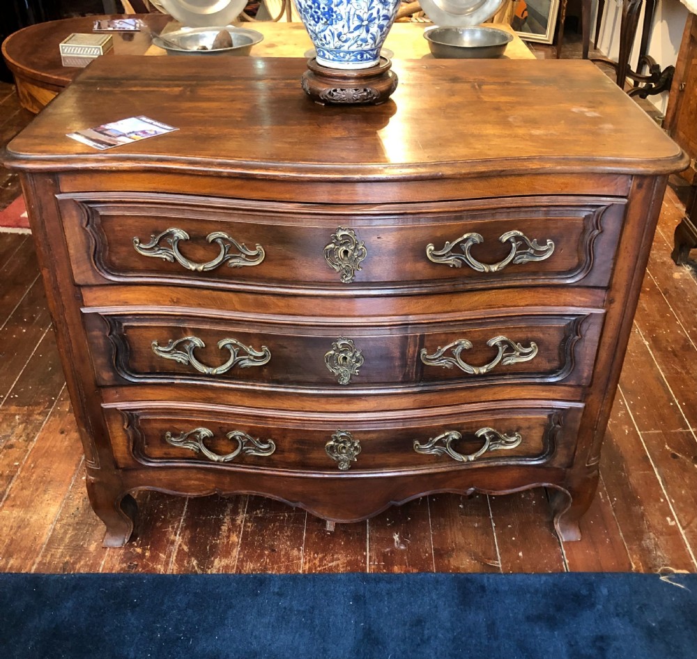 An 18th-century French walnut commode featuring a serpentine front, three drawers with carved moulded frames, cast brass handles, and cabriole legs.