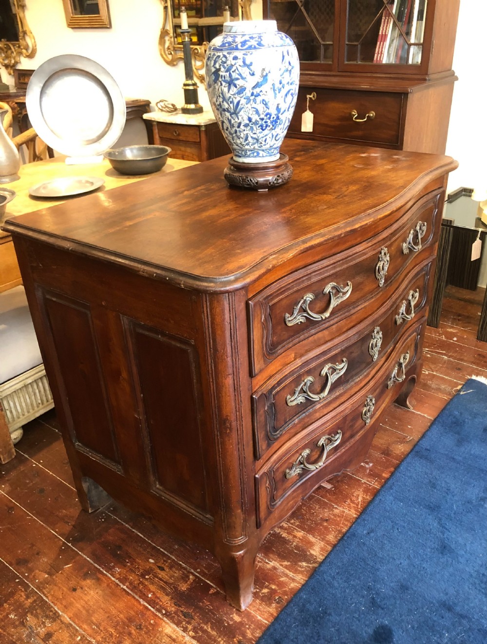 An 18th-century French walnut commode featuring a serpentine front, three drawers with carved moulded frames, cast brass handles, and cabriole legs. View IV
