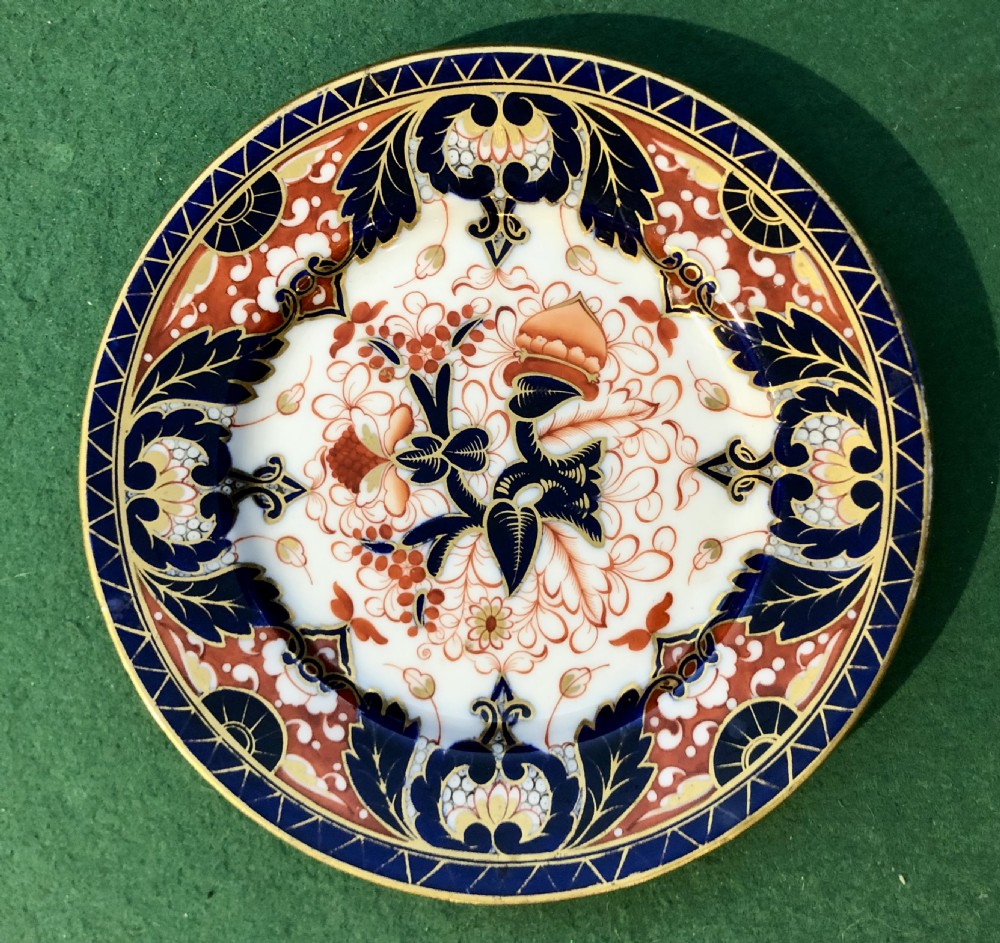 An antique circular porcelain dessert plate decorated with a Japanese-inspired Imari pattern in cobalt blue, terracotta red, and hand-gilded detail.