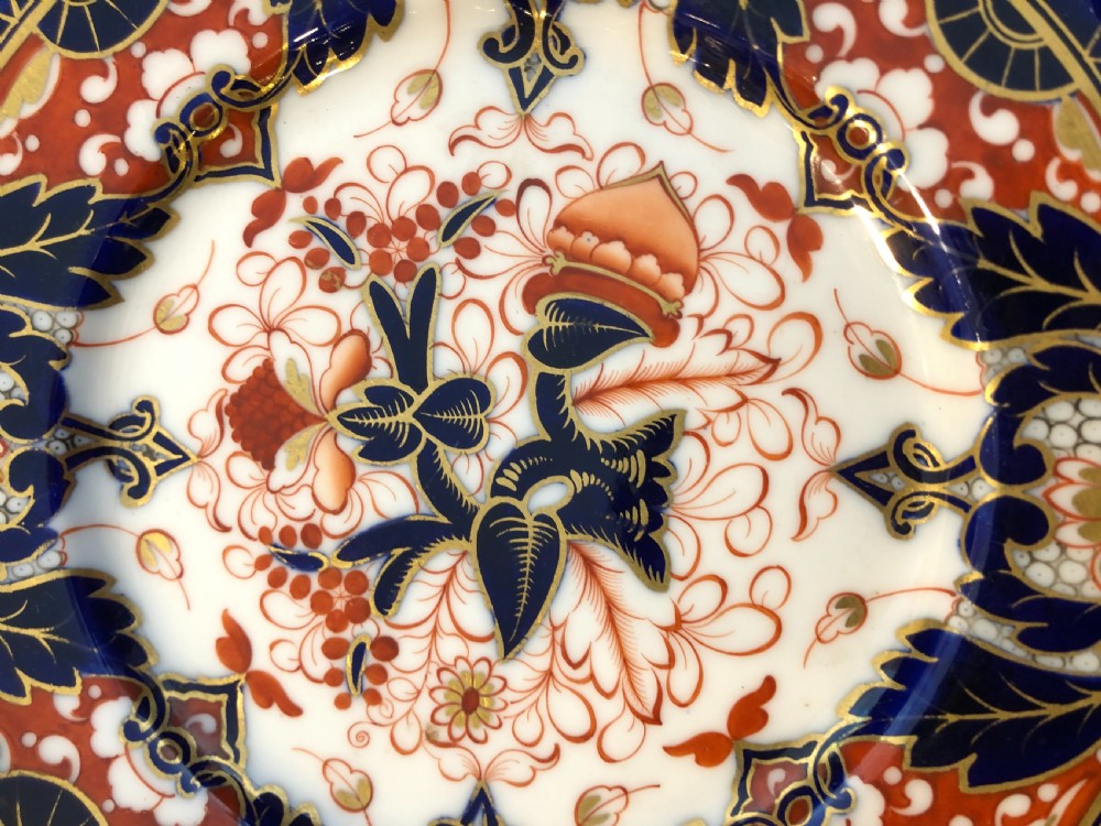 An antique circular porcelain dessert plate decorated with a Japanese-inspired Imari pattern in cobalt blue, terracotta red, and hand-gilded detail. View II