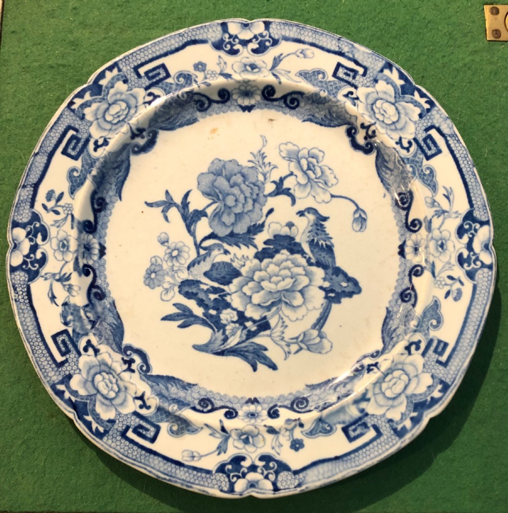 A circular blue and white transfer-printed ceramic plate featuring central floral and bird motifs with a scalloped geometric border.