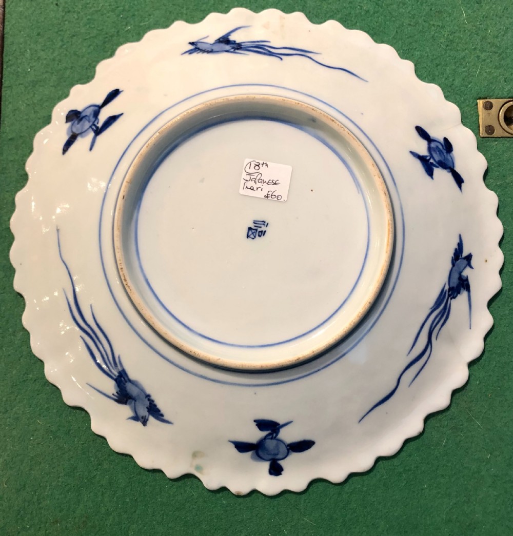 An 18th-century circular Japanese Imari porcelain plate featuring a scalloped rim, cobalt blue and rust red panelled floral patterns, and a central basket motif. View IV