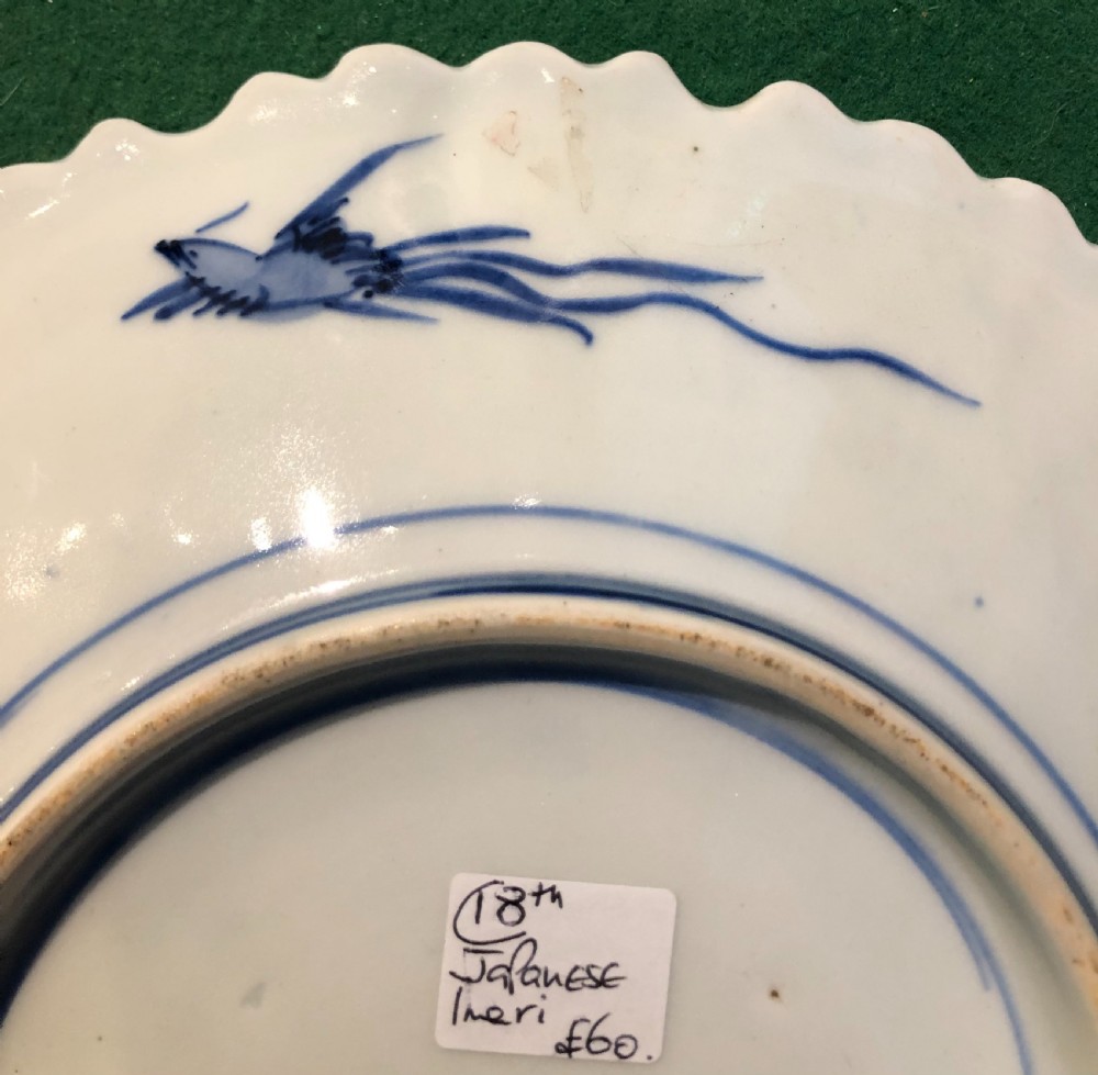 An 18th-century circular Japanese Imari porcelain plate featuring a scalloped rim, cobalt blue and rust red panelled floral patterns, and a central basket motif. View V