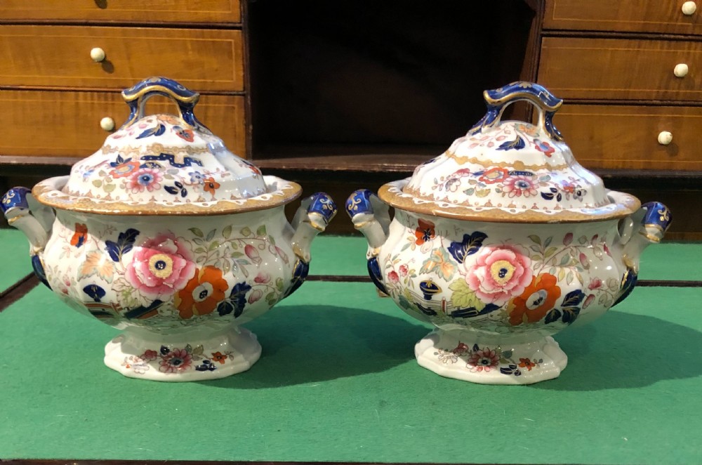 A pair of 19th-century ironstone ceramic tureens with lids, featuring floral hand-painted enamel motifs, cobalt blue handles, and gilt trim.
