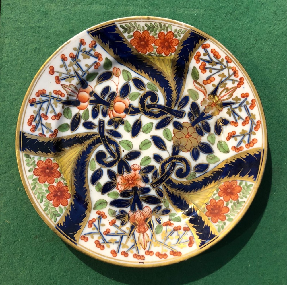 A circular 19th-century Imari style porcelain dessert plate decorated with cobalt blue scrolls, iron red blossoms, green leaves, and gilded accents on a white ground.