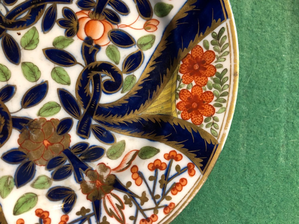 A circular 19th-century Imari style porcelain dessert plate decorated with cobalt blue scrolls, iron red blossoms, green leaves, and gilded accents on a white ground. View II