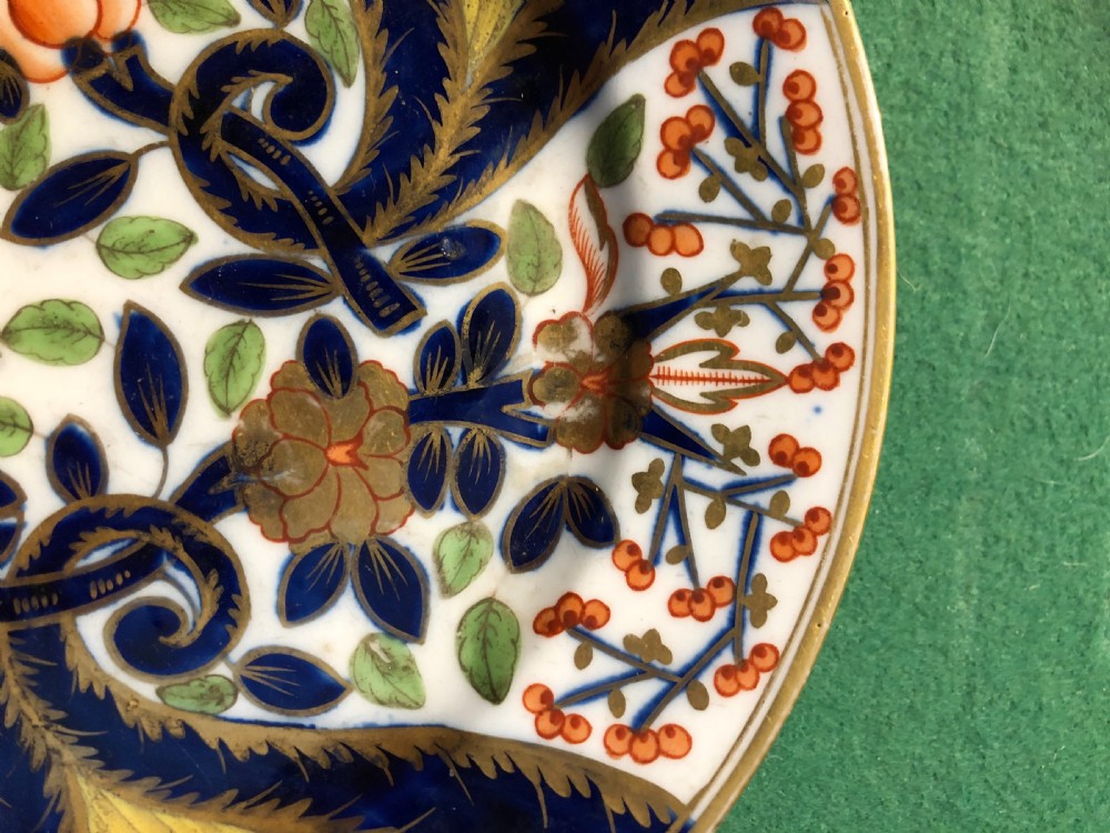 A circular 19th-century Imari style porcelain dessert plate decorated with cobalt blue scrolls, iron red blossoms, green leaves, and gilded accents on a white ground. View III