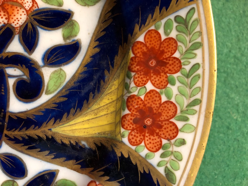 A circular 19th-century Imari style porcelain dessert plate decorated with cobalt blue scrolls, iron red blossoms, green leaves, and gilded accents on a white ground. View IV