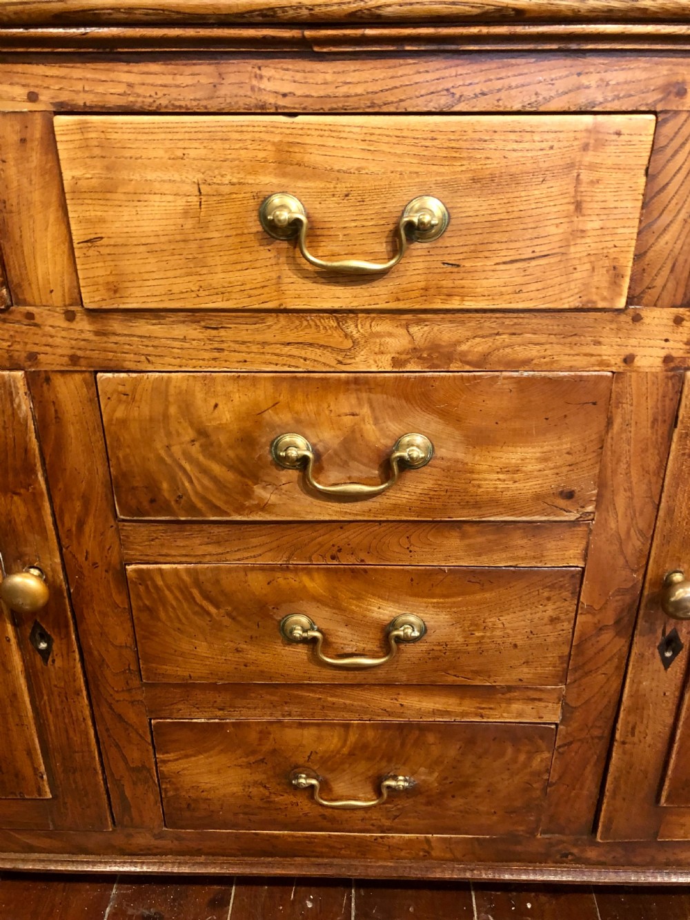 An 18th-century English elm dresser with a three-shelf plate rack, lower drawers with brass handles, and two panelled cupboard doors. View V